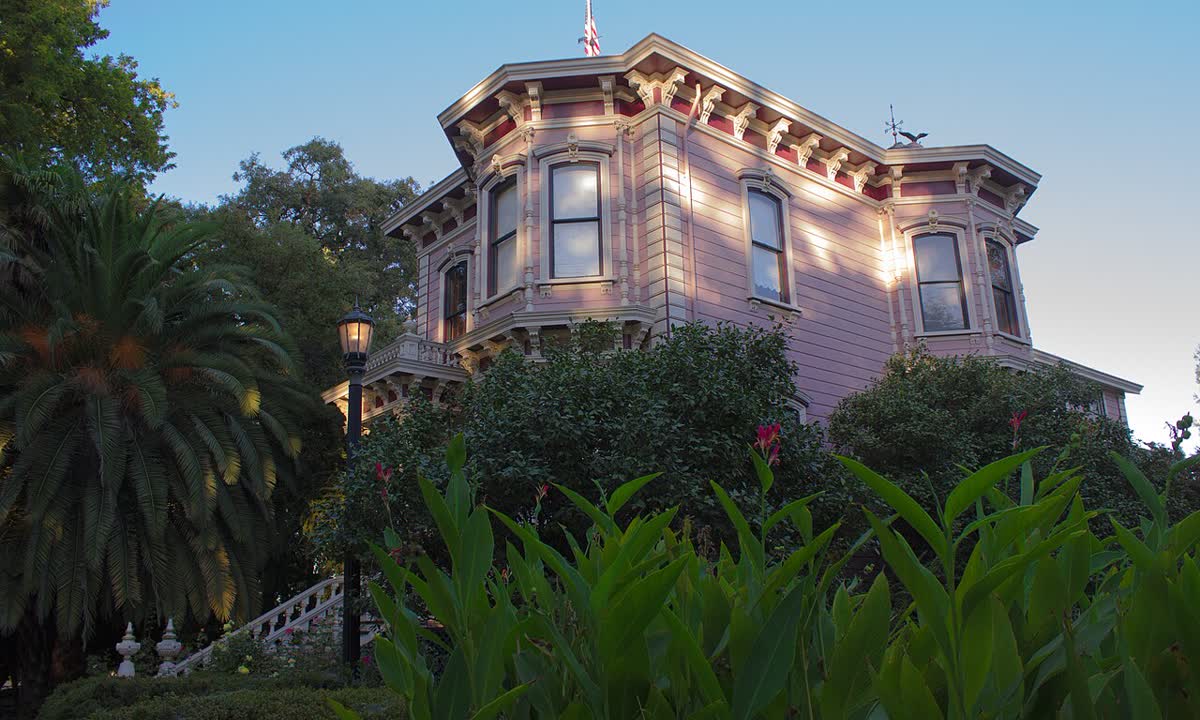 Pink two-story Victorian farmhouse behind palms and shrubs in Sacramento County